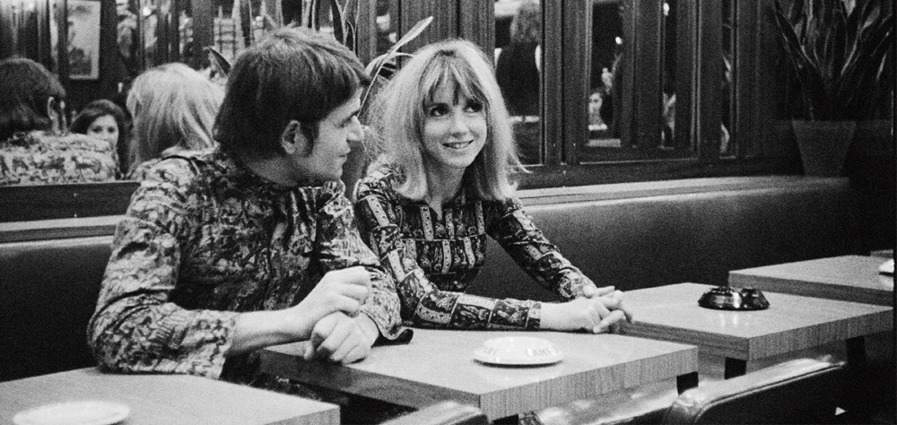 Cena em preto e branco mostra um casal sentado à mesa de um restaurante.